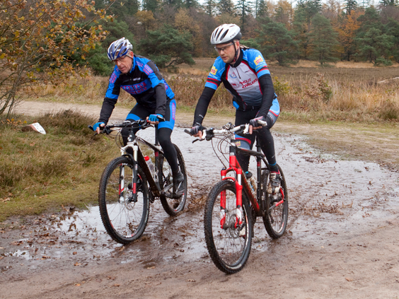 Twee mountainbikers rijden door de modder op een uitdagend parcours in de bossen van Drenthe, in de omgeving van Landal het Land van Bartje.