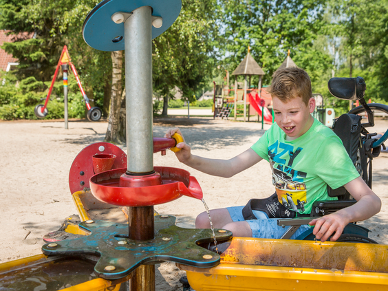 Een jongen in een rolstoel speelt met een water- en zandspeeltoestel in de toegankelijke buitenspeeltuin van Landal het Land van Bartje.