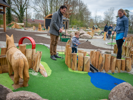 Gezin met een jong kind speelt midgetgolf op de avontuurlijke midgetgolfbaan met houten obstakels op vakantiepark Landal het Land van Bartje.