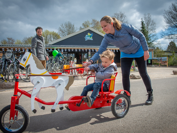 Een moeder helpt haar zoontje op een paardjes-skelter bij de fietsverhuur van Landal het Land van Bartje, klaar om het park te verkennen.