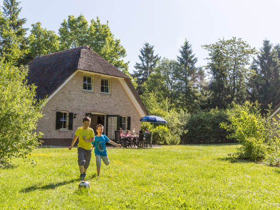 Twee jongens voetballen in de grote, groene tuin voor hun Drentse boerderij accommodatie op vakantiepark Landal het Land van Bartje.