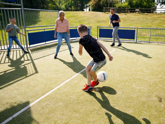 Een gezin speelt een partijtje voetbal in de pannakooi op het kunstgrasveld van het sportieve vakantiepark Landal het Land van Bartje.