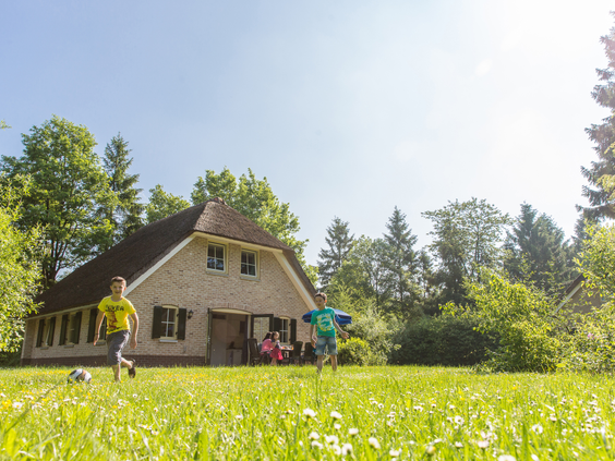 Kinderen spelen in de zon op het grasveld voor hun vrijstaande Drentse boerderij op vakantiepark Landal het Land van Bartje.