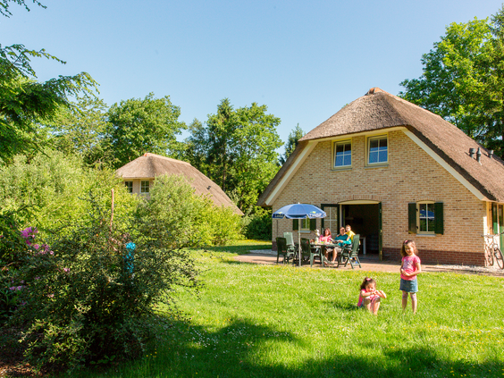 Een gezin geniet van het buitenleven in de ruime tuin bij hun authentieke Drentse boerderij met rieten dak op vakantiepark Landal het Land van Bartje.