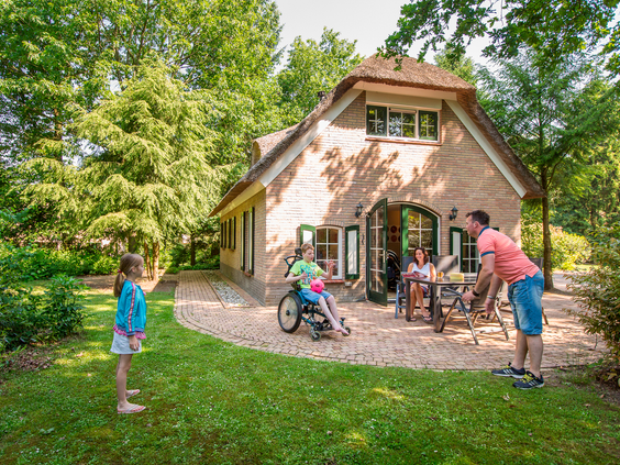 Een gezin, inclusief een kind in een rolstoel, geniet samen op het terras van hun speciaal aangepaste, toegankelijke bungalow op Landal het Land van Bartje.