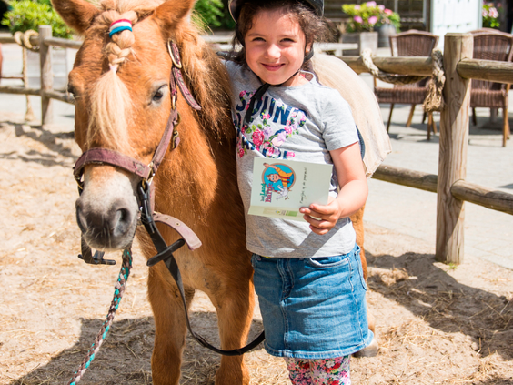 Een trots meisje knuffelt haar pony op de ponyranch van Landal het Land van Bartje en laat haar ponyverzorgingsdiploma zien.