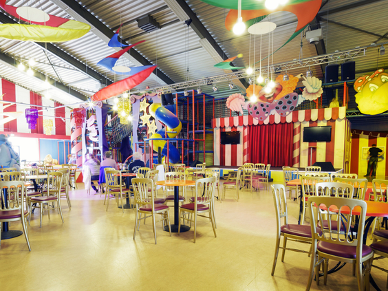 Het ruime en kleurrijke zitgedeelte voor ouders bij het indoorspeelparadijs van Landal Aelderholt, met uitzicht op de speeltoestellen.