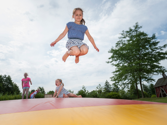 Kinderen maken hoge sprongen in de lucht op de grote, opblaasbare airtrampoline in de buitenspeeltuin van Landal Aelderholt.