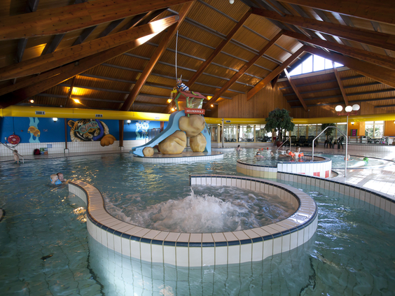 Het overdekte zwembad van Landal Aelderholt met een groot bubbelbad op de voorgrond en een waterglijbaan en stroomversnelling op de achtergrond.