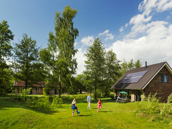 Kinderen spelen en rennen op een groot, groen grasveld voor een vrijstaande bungalow met zonnepanelen op vakantiepark Landal Aelderholt.