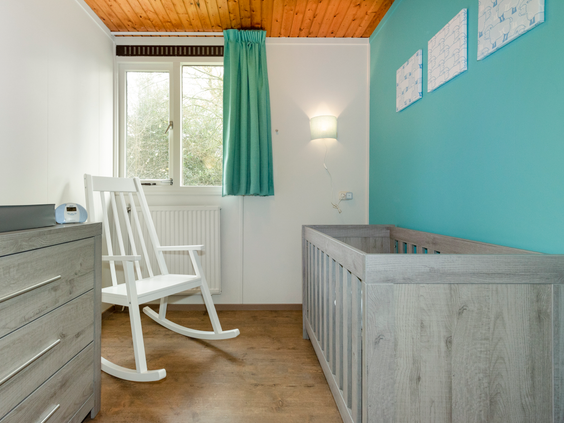 Een speciale babykamer in een kinderbungalow op Landal Aelderholt, compleet ingericht met een kinderbedje, commode en een witte schommelstoel.