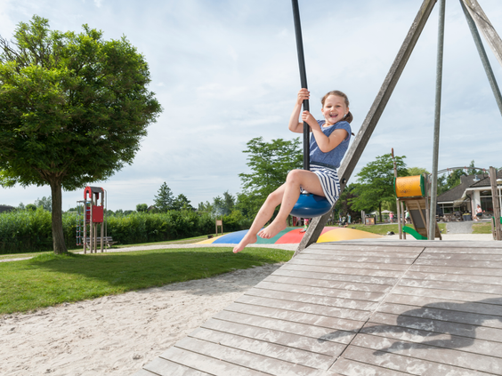 Een blij meisje zoeft met hoge snelheid van de kabelbaan in de grote buitenspeeltuin van vakantiepark Landal Aelderholt.
