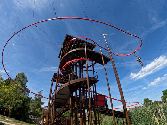 De hoge, stalen klimtoren skyflyer van het klim- en avonturenpark op Landal Aelderholt, waar de rode tokkelbaan omheen en vanaf slingert.