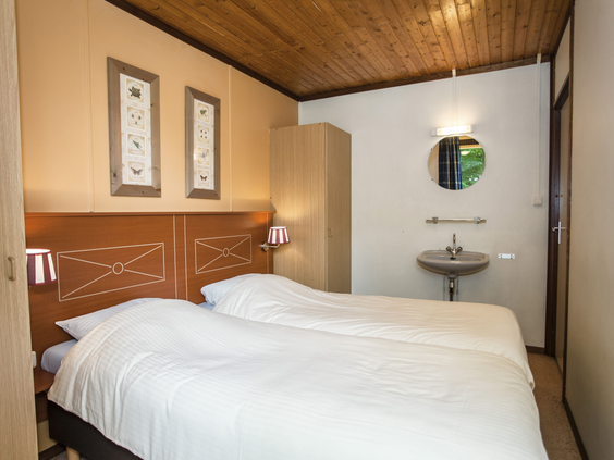 Een netjes opgemaakt tweepersoonsbed in een sfeervolle slaapkamer met houten details en een eigen wastafel in een bungalow op Landal Aelderholt.