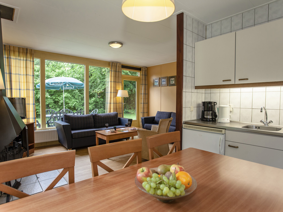 De open keuken en eethoek in een bungalow op Landal Aelderholt, met een houten eettafel en uitzicht op de zithoek en de groene tuin.