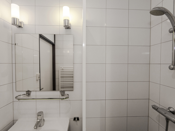 Een moderne badkamer met witte tegels, een wastafel, spiegel en een ruime inloopdouche in een bungalow op Landal Aelderholt in Drenthe.