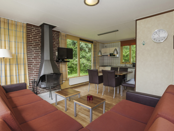 Een grote, open woonkamer van een groepsaccommodatie op Landal Sluftervallei, waar een familie ontspant op de banken en aan de lange eettafel.