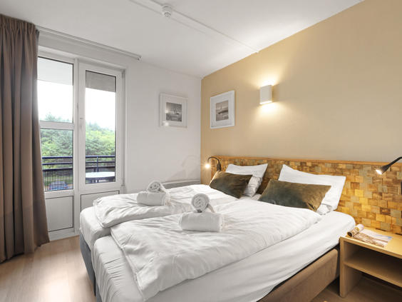 Comfortabele slaapkamer met een opgemaakt tweepersoonsbed en toegang tot het balkon in een appartement van Landal Ameland State.