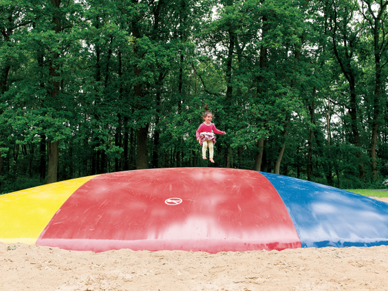Een kind springt hoog in de lucht op de grote, kleurrijke airtrampoline, omringd door het bos van Landal Amerongse Berg.