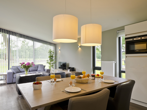 De sfeervolle en ruime woonkamer van een bungalow op Landal Amerongse Berg, met een grote eettafel en uitzicht op de natuur.