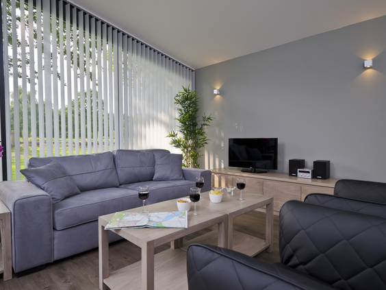 De lichte en moderne woonkamer van een bungalow op Landal Amerongse Berg, met een comfortabele grijze hoekbank en fauteuils.
