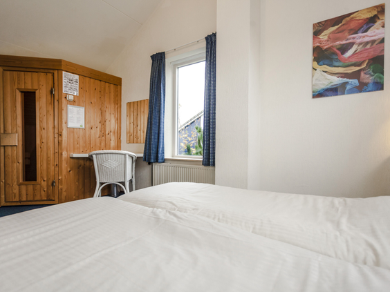 Slaapkamer met een opgemaakt bed en een ingebouwde privé-sauna in een luxe villa op Landal Beach Park Texel.