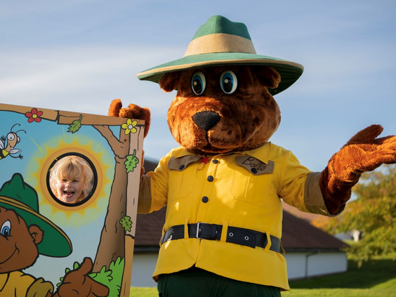Landal mascotte Bollo de Beer staat naast een fotobord waar een kind doorheen kijkt voor een leuke foto.