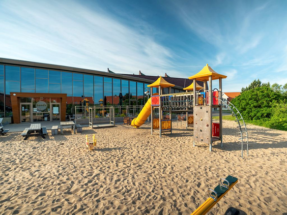 Grote zandspeeltuin bij het centrumgebouw van Landal Beach Resort Ooghdyne, met een kleurrijk klimtoestel met glijbaan en klimwand.