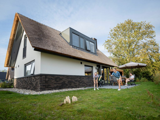 Een familie ontspant op het terras van een moderne, rietgedekte duinvilla met grote tuin op vakantiepark Landal Berger Duinen.