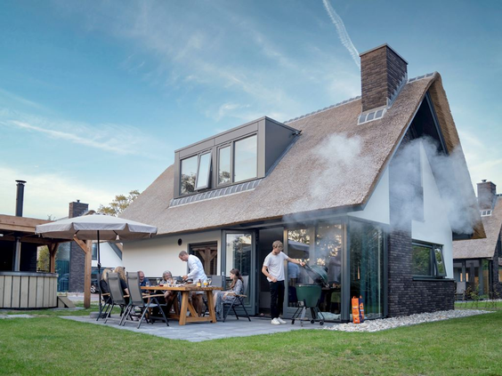 Een gezin geniet van een barbecue op het overdekte terras van hun luxe vakantiehuis met rieten dak op Landal Berger Duinen.