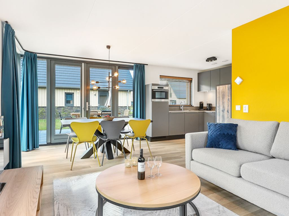 Het moderne en kleurrijke interieur van de woonkamer van een vakantievilla op Landal Berger Duinen, met een open keuken.