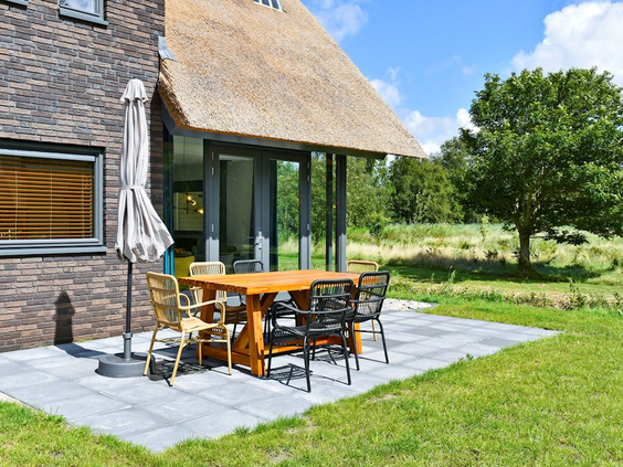 Het zonnige terras met een houten tuinset en parasol van een rietgedekte vakantievilla op Landal Berger Duinen.