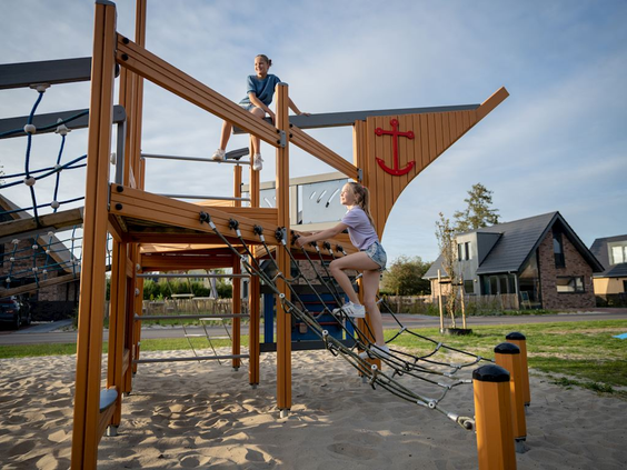 Twee kinderen klimmen en klauteren op een avontuurlijk houten speeltoestel in de vorm van een schip in de speeltuin van Landal Berger Duinen.