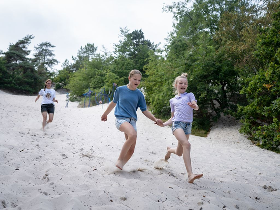 Drie kinderen rennen en spelen op blote voeten in het mulle zand van de Schoorlse Duinen, nabij Landal Berger Duinen.