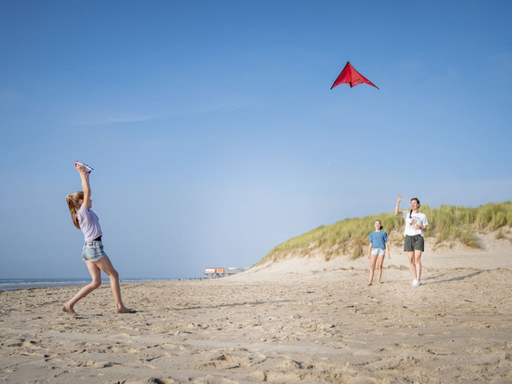Een familie laat een rode vlieger op aan het brede zandstrand van Bergen aan Zee, vlak bij de Noord-Hollandse duinen.