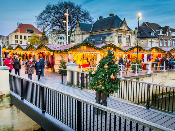 De sfeervolle kerstmarkt in het centrum van Valkenburg, met verlichte kraampjes, een kerstboom en bezoekers op een brug.