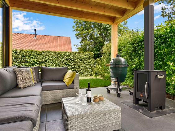 Een luxe, overdekt terras met een comfortabele loungeset, een Green Egg barbecue en een buitenhaard bij een vakantiewoning op Landal Cauberg.