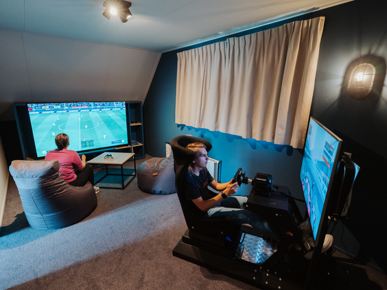 Een speciale gameroom in een vakantiehuis op Landal Cauberg, uitgerust met grote tv-schermen, zitzakken en een professionele race-simulator.