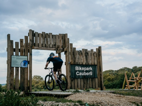 Een mountainbiker rijdt door de houten toegangspoort van Bikepark Cauberg, gelegen naast vakantiepark Landal Cauberg.