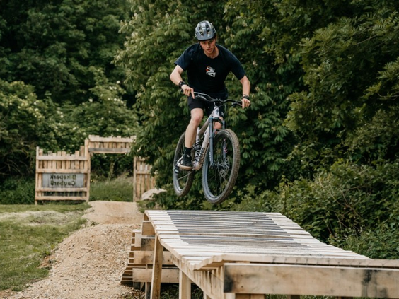 Een mountainbiker maakt een hoge sprong over een houten schans in het avontuurlijke Bikepark Cauberg in Valkenburg.
