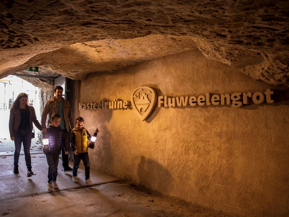 Een gezin met kinderen en zaklampen staat bij de ingang van de historische Fluweelengrot in Valkenburg, klaar voor een rondleiding.