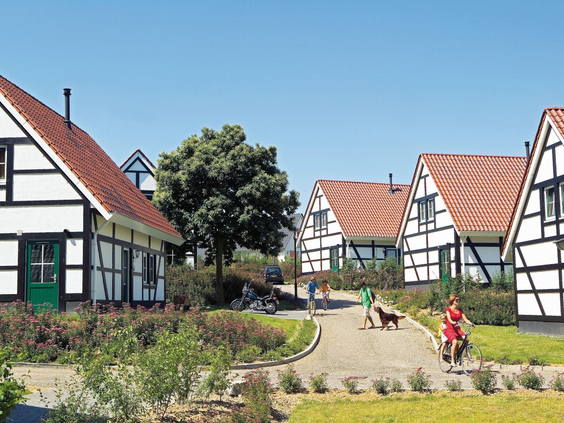 Gasten wandelen langs de karakteristieke wit met zwarte vakwerkhuizen op een zonnige dag op vakantiepark Landal Cauberg.