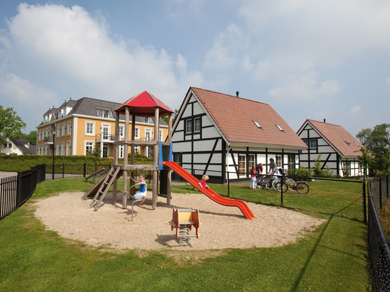 Een leuke speeltuin met een glijbaan en klimrek in een zandbak op het vakantiepark Landal Cauberg, gelegen tussen de vakwerkhuizen.