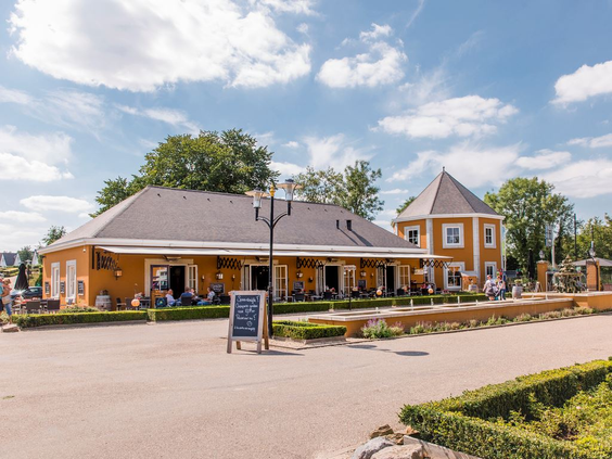 Het zonnige terras en het okergele receptiegebouw van vakantiepark Landal Cauberg, bovenop de Cauberg in Valkenburg.