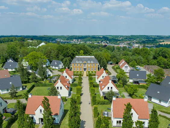Luchtfoto van vakantiepark Landal Cauberg met de witte villa's en het statige hoofdgebouw, gelegen in het heuvelachtige Limburgse landschap.