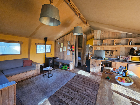 Het sfeervolle houten interieur van een luxe safaritent op Landal Coldenhove, met een woonkamer en keuken.