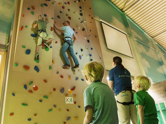 Kinderen klimmen op de hoge indoor klimwand van Landal Coldenhove, onder begeleiding van een instructeur.