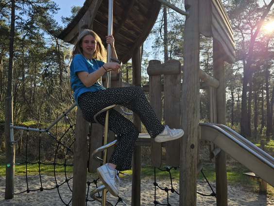 Een meisje klautert op een houten speeltoestel in de avontuurlijke buitenspeeltuin van Landal Coldenhove, midden in het bos.
