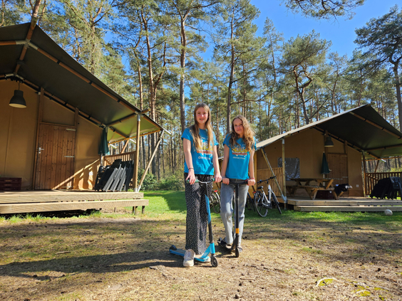 Twee meiden met een step voor de safaritenten op Landal Coldenhove, midden in de bossen van de Veluwe.