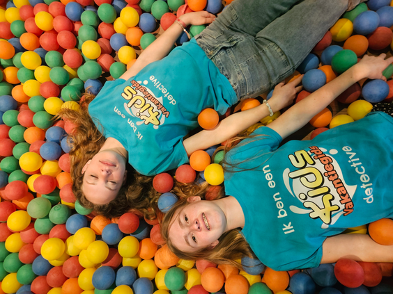 Twee meiden liggen lachend in de kleurrijke ballenbak van de binnenspeeltuin op Landal Coldenhove.